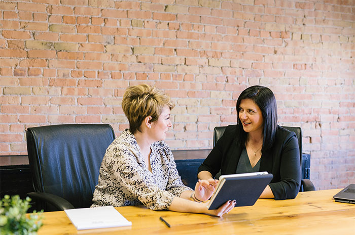 Two HR employees discussing a background check on a tablet in an office with a brick wall background