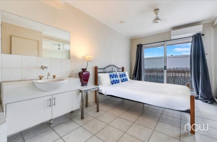 Small rental bedroom with bed, sink, tiled floor, air conditioning, and sliding door, illustrating bad landlords' poor housing.