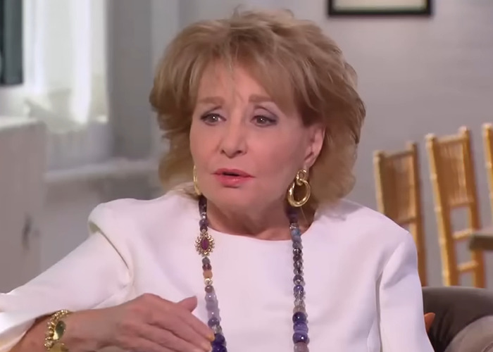 Barbara Walters in an interview setting, wearing a white outfit and colorful necklace, engaging in a serious conversation. Barbara Walters in an interview setting, wearing a white outfit and colorful necklace, engaging in a serious conversation.