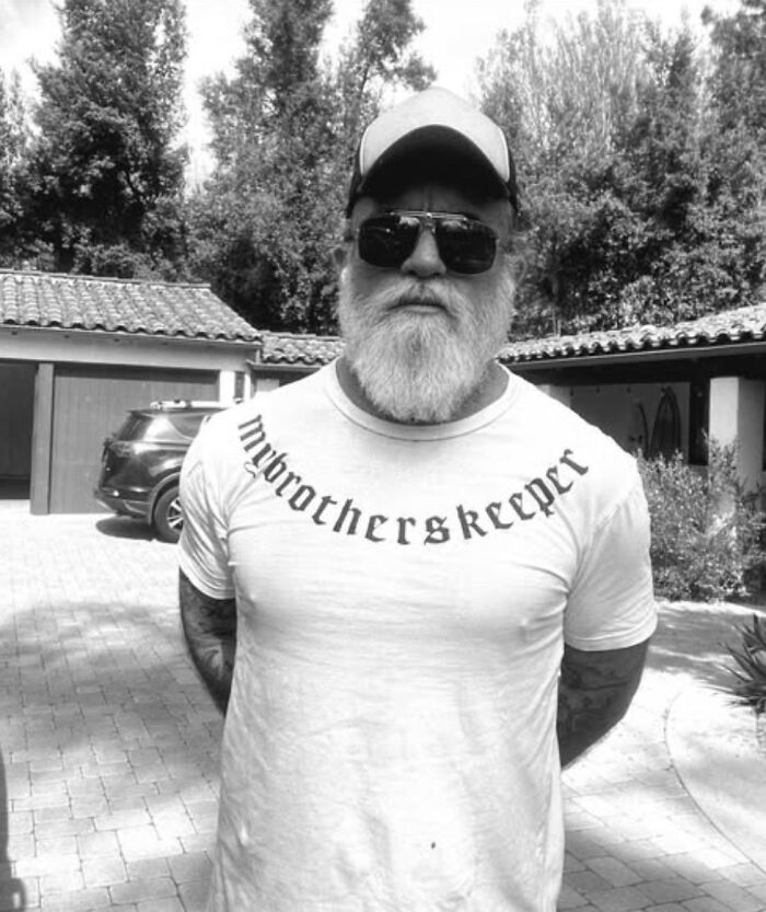 Prison Break star Dominic Purcell with a full white beard, sunglasses, and a cap in an outdoor driveway setting.
