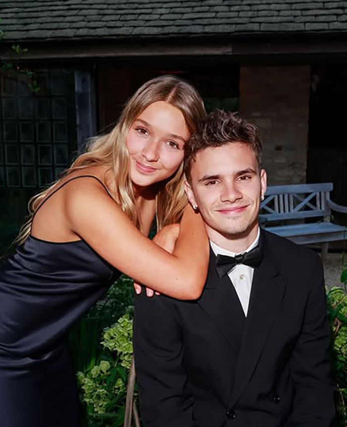 Young woman in black dress hugging man in tuxedo at David Beckham's 50th birthday party amid family feud photos.