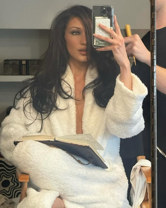 Bella Hadid taking a mirror selfie wearing a white robe while preparing for Cannes Film Festival revealing dress event.