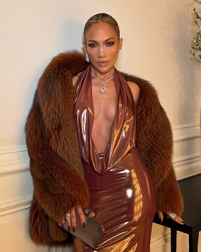 Jennifer Lopez wearing a shiny brown dress and fur coat, accessorized with diamond jewelry and holding a clutch bag indoors. Jennifer Lopez wearing a shiny brown dress and fur coat, accessorized with diamond jewelry and holding a clutch bag indoors.