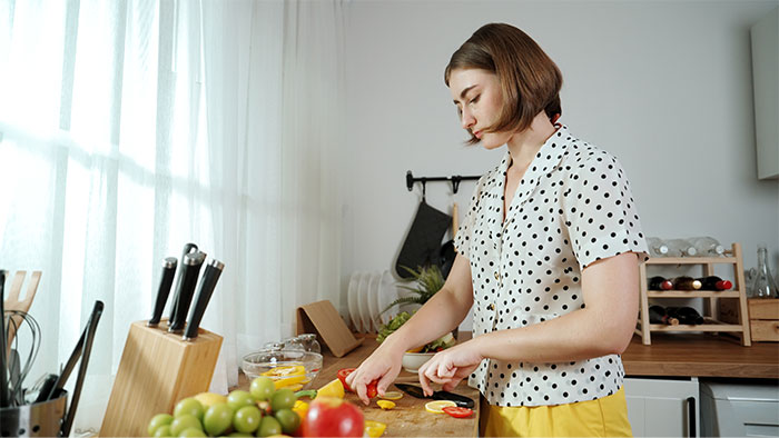 Young woman preparing dinner in a kitchen, focused on cutting vegetables late at night in a casual setting Young woman preparing dinner in a kitchen, focused on cutting vegetables late at night in a casual setting