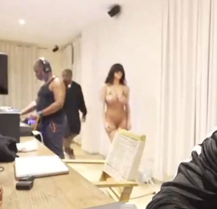 Kanye West's friend covering camera quickly while Bianca Censori struts in wearing minimal clothing indoors.