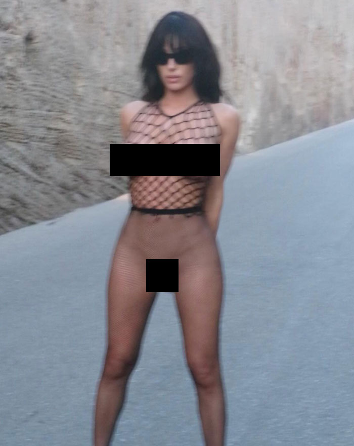 Bianca Censori in a sheer fishnet outfit posing outdoors as public calls for arrest over indecency grow louder.
