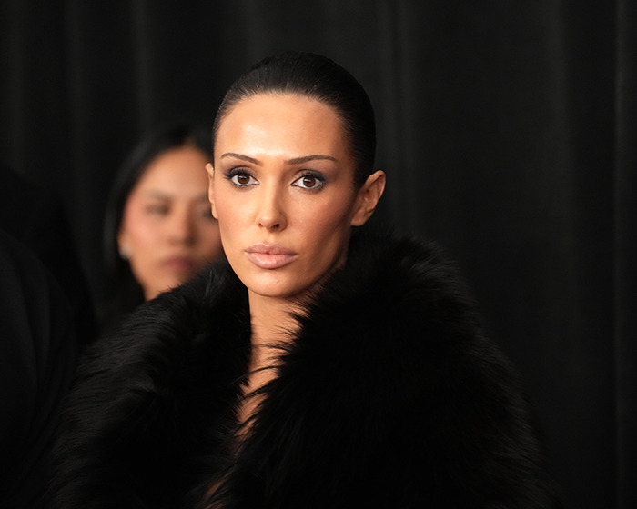 Woman with slicked-back hair wearing a black fur coat, posing confidently after sparking outrage with a racy outfit.