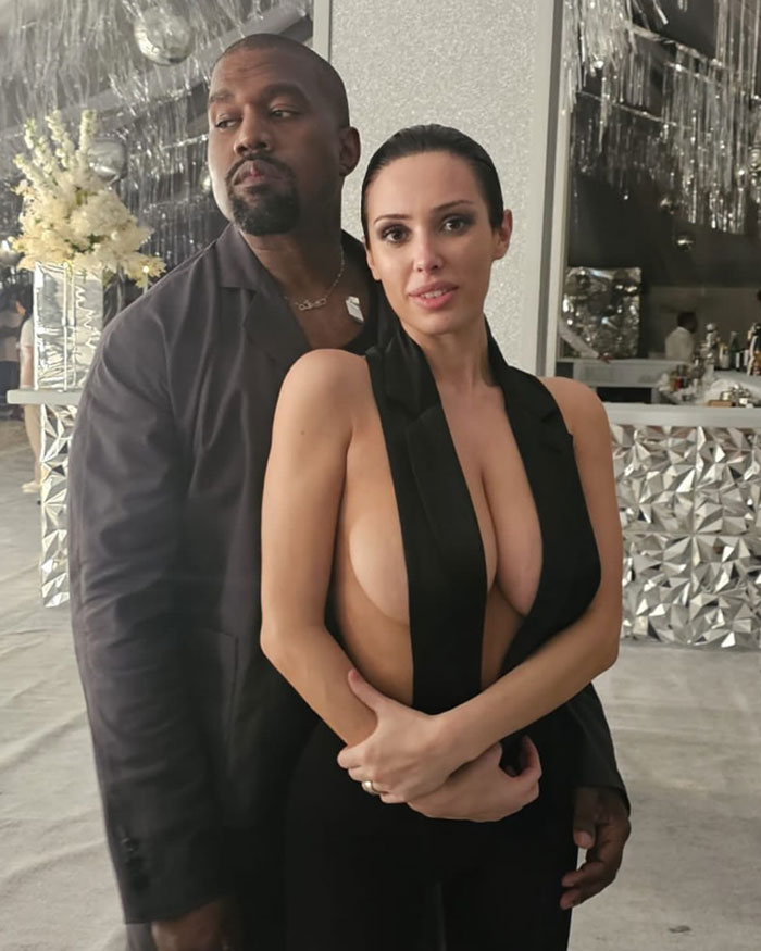 Kanye West with Bianca Censori in a stylish setting, Bianca wearing a revealing black outfit.