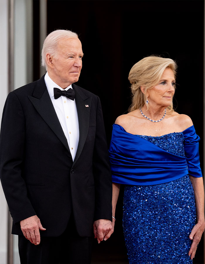 Former President Biden and Jill Biden holding hands, dressed formally, amid reports of aggressive prostate cancer bone spread.