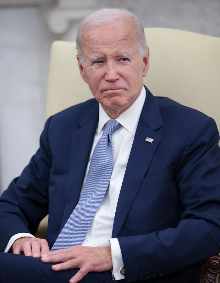 Former President Biden sitting in a chair wearing a suit and tie, facing health challenges with aggressive prostate cancer.