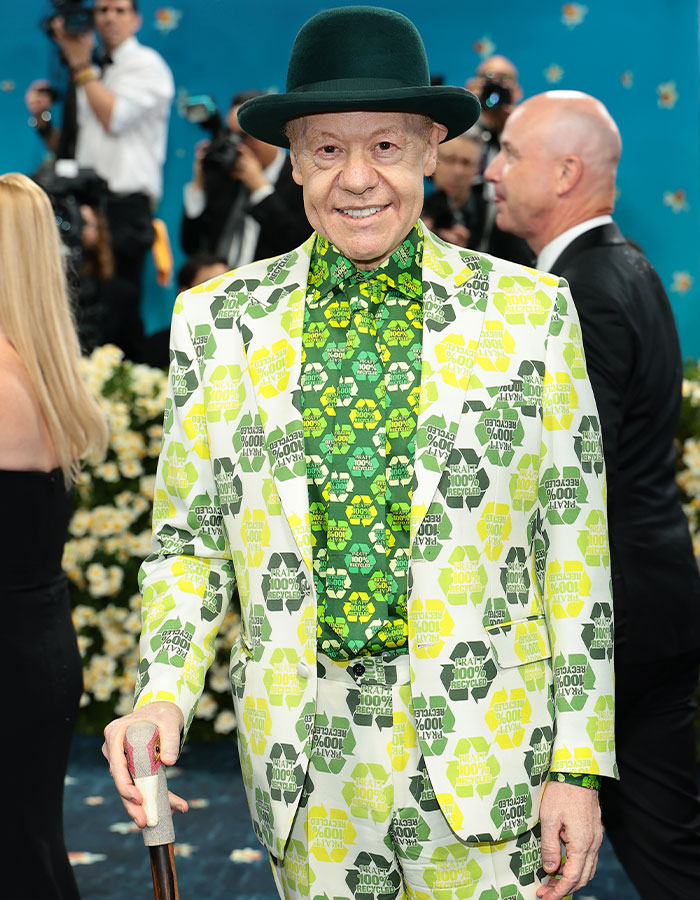 Man wearing mismatched green and yellow printed suit and hat, posing at a notable event highlighting fashion fails.