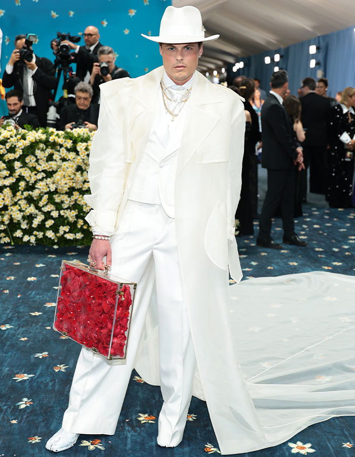 Man in all-white oversized suit and hat holding a red floral bag at Met Gala 2025 fashion fails event.