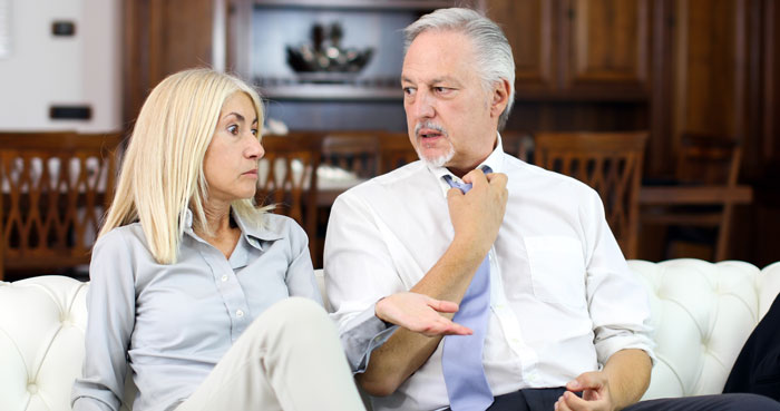 Middle-aged man and woman sitting on a couch having a tense conversation about front-row seat to daughter's delivery.