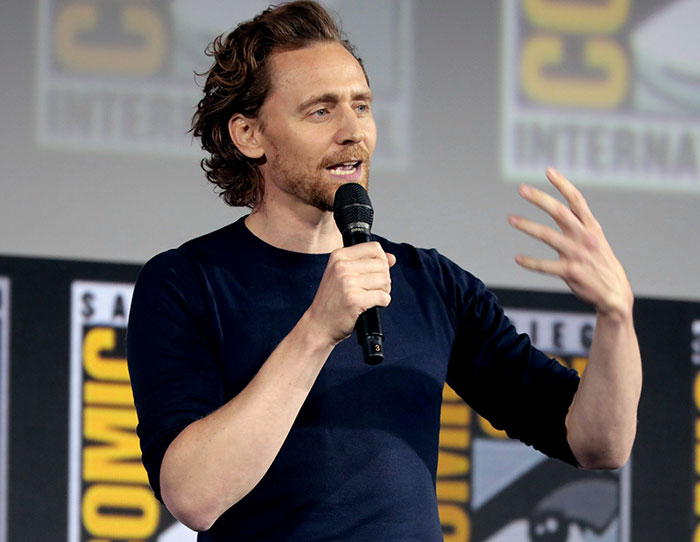 Actor speaking on stage at a Comic-Con event, sharing stories about the strangest ways people crossed paths with celebs.