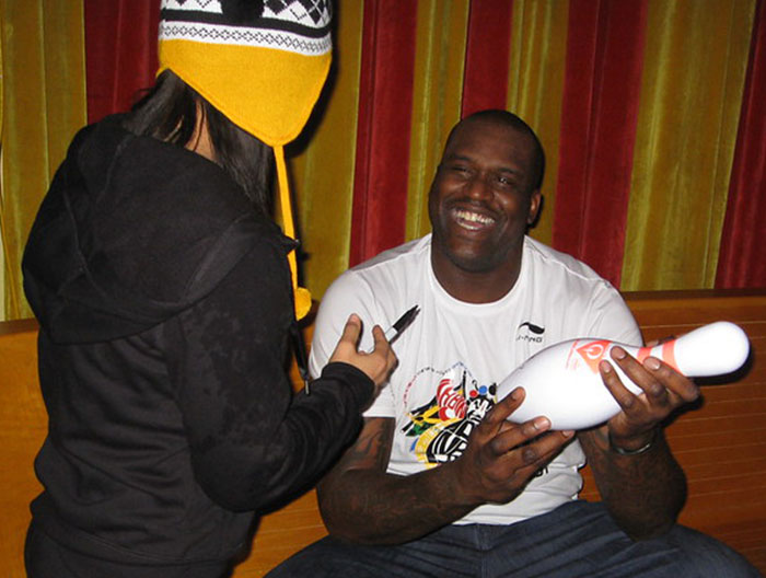 Man smiling and holding a bowling pin while signing autographs during a casual celebrity meet and greet encounter