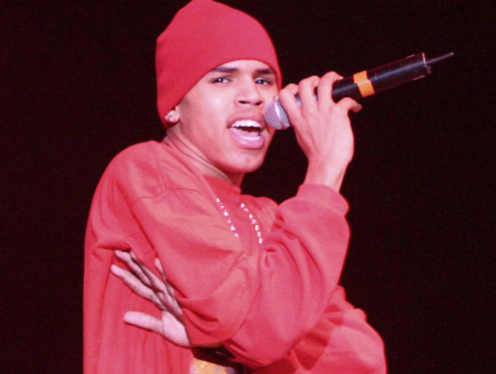 Male performer in a red hat and sweater singing into a microphone, illustrating strange ways people cross paths with celebs.