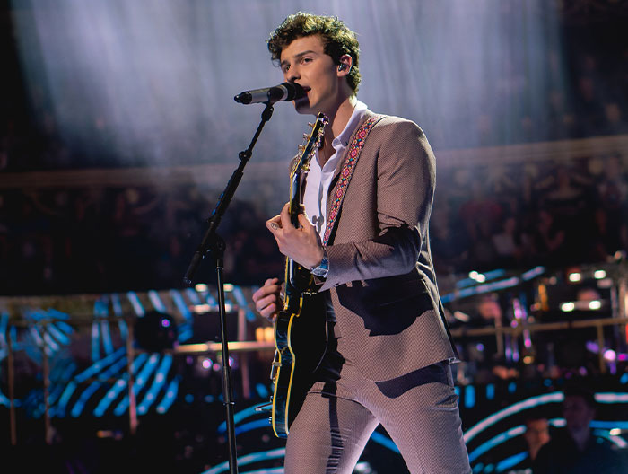 Male musician performing on stage with guitar and microphone, highlighting stranger ways people crossed paths with celebs.