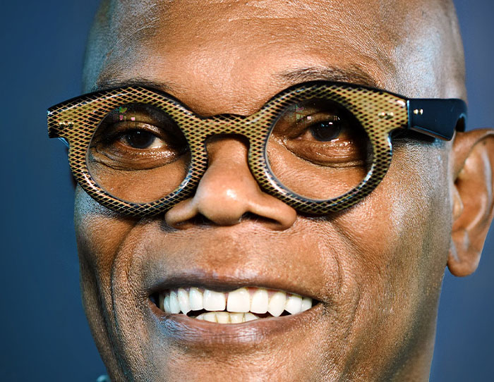 Close-up of a smiling man wearing distinctive glasses, illustrating strange ways people have crossed paths with celebs.