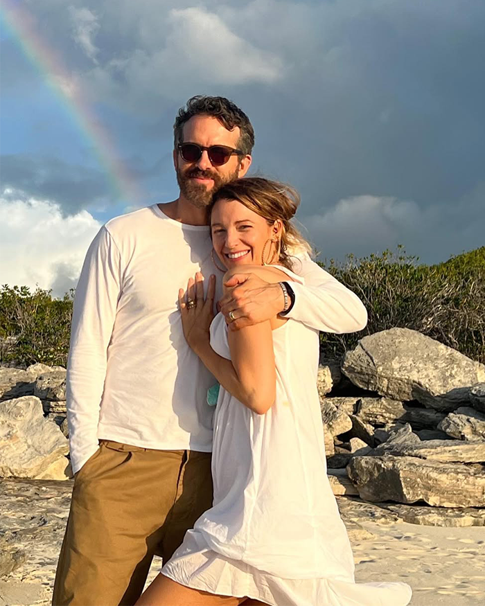 Couple embracing near rocky shore with rainbow in background, related to Scarlett Johansson, Ryan Reynolds, and Blake Lively lawsuit.
