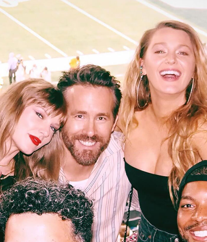 Taylor Swift and Blake Lively smiling with friends at an outdoor event, capturing a joyful moment together.