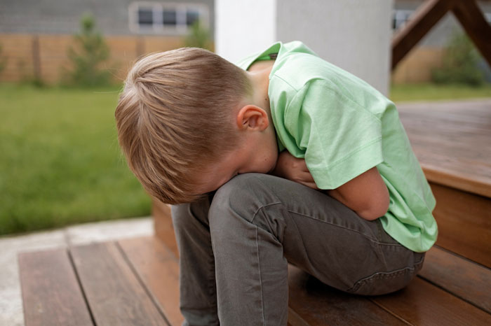 Young boy sitting on wooden steps with head down, representing neighbor’s kid turning fence into fast food window for dogs. Young boy sitting on wooden steps with head down, representing neighbor’s kid turning fence into fast food window for dogs.