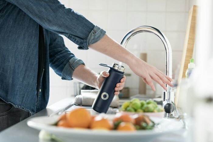 Person reaching to turn on kitchen faucet while holding a water bottle, demonstrating excessive laziness at home.