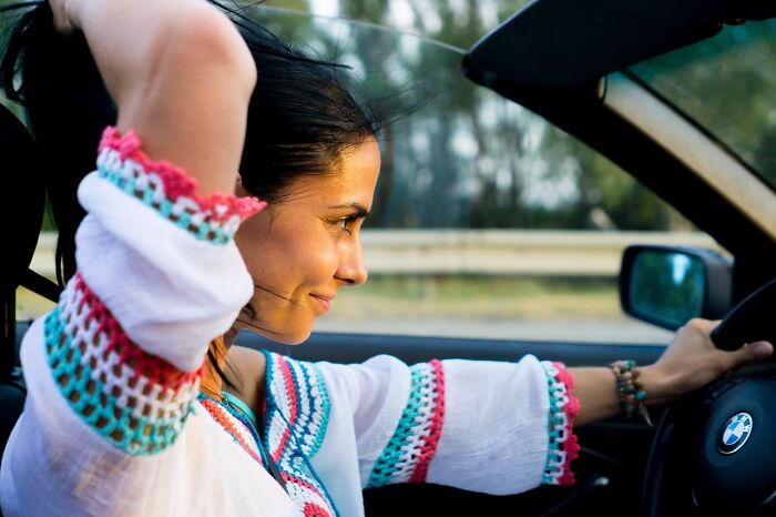 Woman smiling while driving a car, enjoying low-key pleasures that bring simple happiness and contentment.