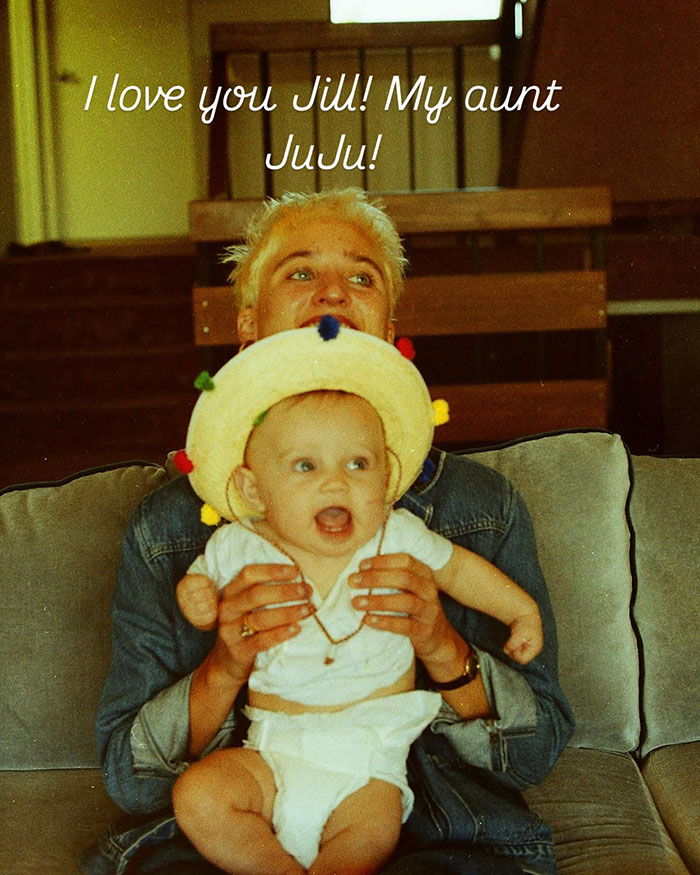 Singer Jill Sobule with a baby, sitting on a couch, wearing a denim jacket and a playful hat. Singer Jill Sobule with a baby, sitting on a couch, wearing a denim jacket and a playful hat.