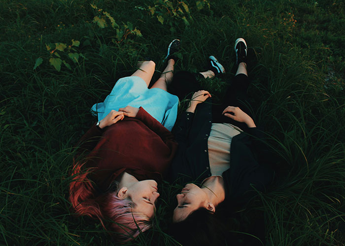 Two women lying on grass close together, illustrating a story about a guy always bringing his BFF to dates.