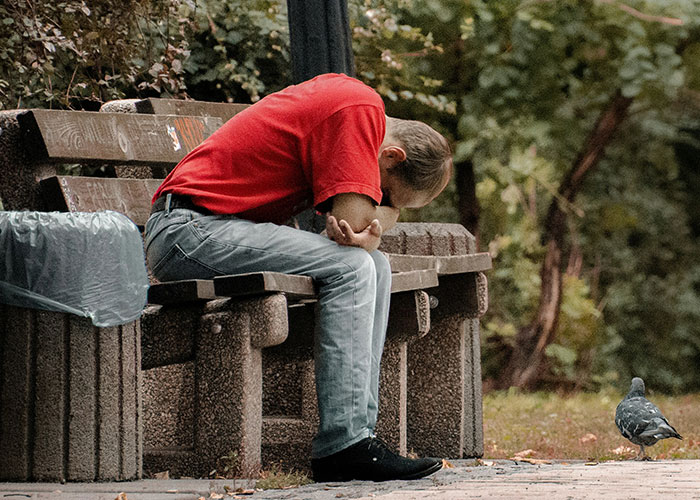 Man in red shirt sitting on park bench looking upset, reflecting on guy always bringing BFF to dates unhinged truth.
