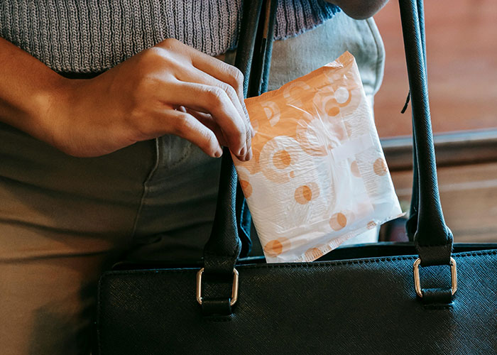 Woman placing a period pad into a black handbag, highlighting issues about dumping boyfriend over refusal to hand items. Woman placing a period pad into a black handbag, highlighting issues about dumping boyfriend over refusal to hand items.