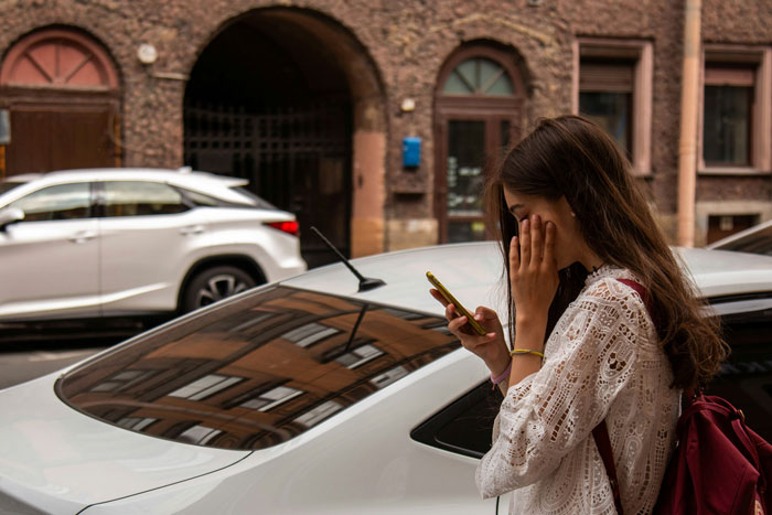 Young woman outside near cars, looking upset while checking her phone, relating to song performance connection conflict.