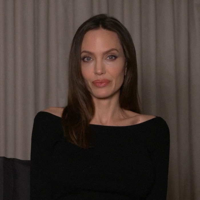 Angelina Jolie seated wearing a black top against a neutral backdrop, related to Brad Pitt divorce battle update.