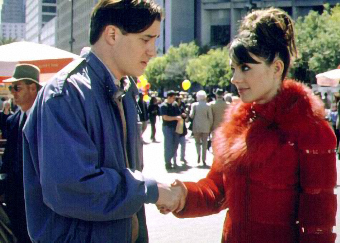 Brendan Fraser with a slimmed down physique shaking hands with a woman in a red coat at an outdoor event.