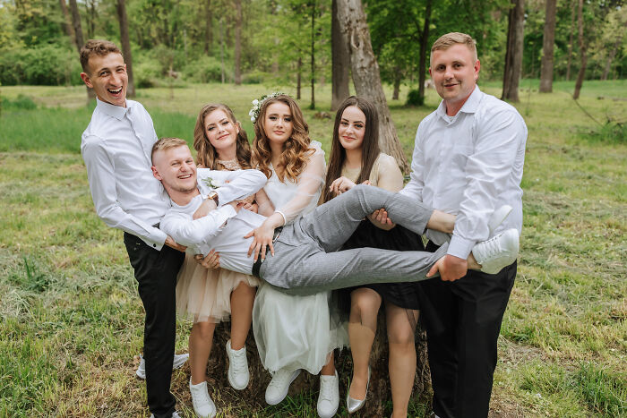 Group of young adults outdoors, smiling and playfully lifting a friend, capturing moments that feel like being picked last in gym class.