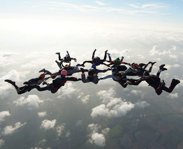 Group of experienced skydivers in formation above clouds during a high-altitude jump on a clear day.