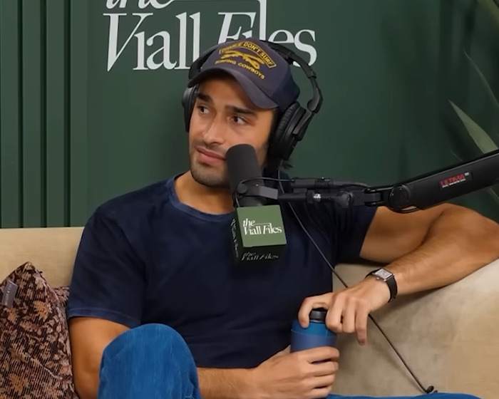 Sam Asghari wearing a baseball cap and headphones, speaking into a microphone during a podcast recording session.