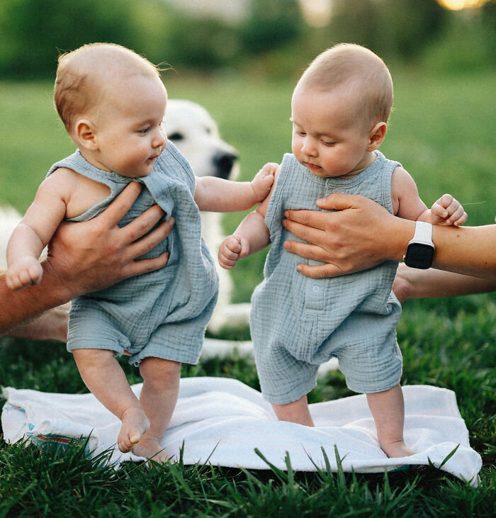 Two babies in matching outfits held by adults on a blanket outside, illustrating hilariously bad names topic.