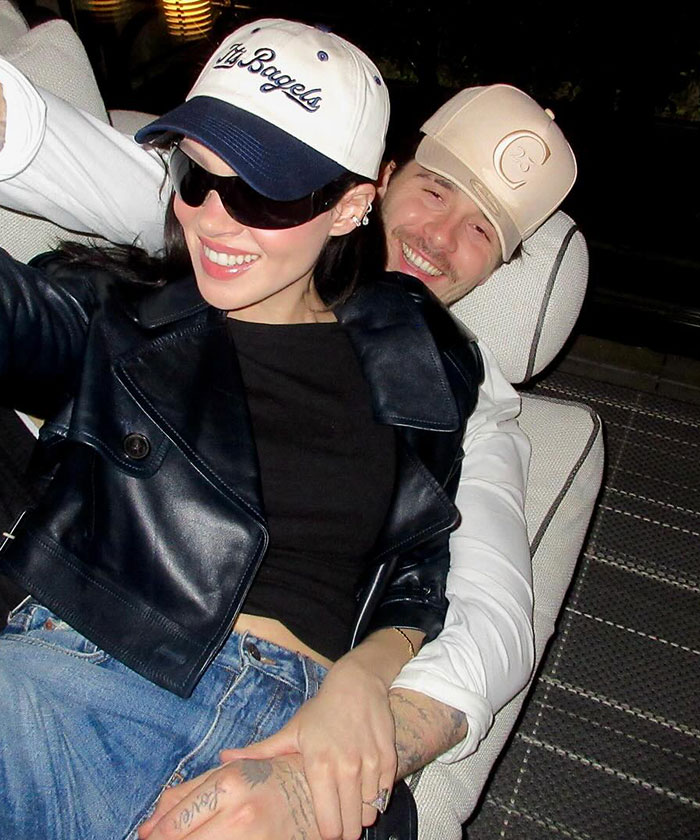 Couple wearing caps and casual clothes, smiling and sitting closely, reflecting a moment at David Beckham's birthday party feud.