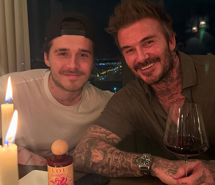 Two men smiling at a dinner table with drinks, related to Brooklyn Beckham's ex and Beckham family discussion.