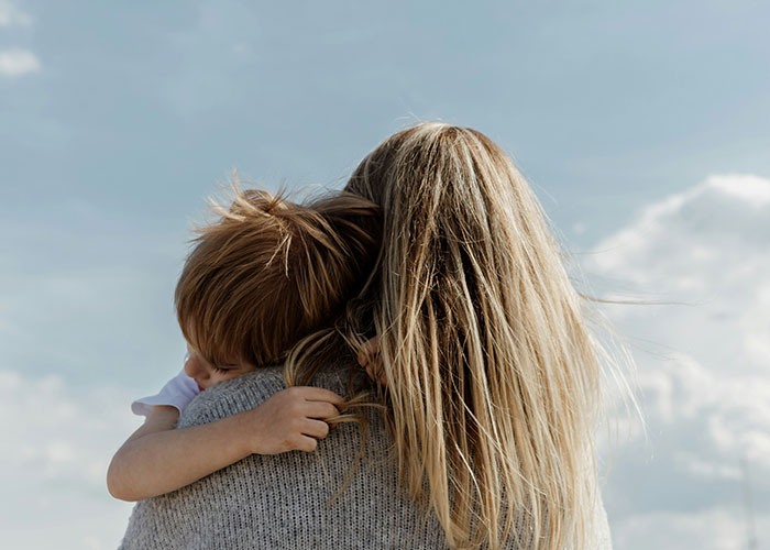 Woman with long blonde hair holding a young child outdoors, illustrating challenges of treating kids equally in blended families.
