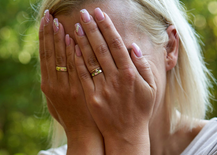 Woman with blonde hair covering her face with hands, reflecting emotions related to family and children treatment conflict.