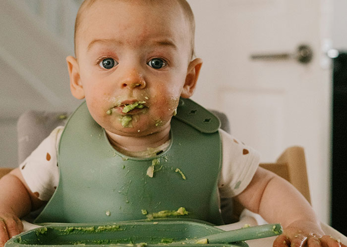 Baby wearing a green bib with food smeared on face and tray, illustrating treating kids in family dynamics.