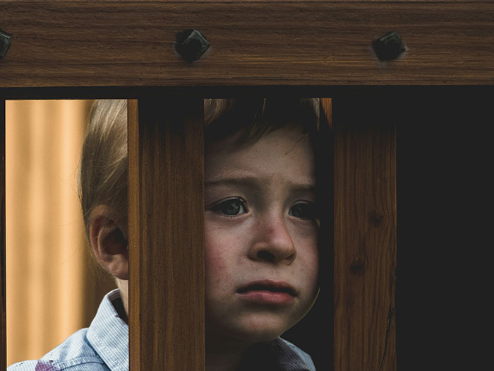 Young child looking sad and thoughtful behind wooden bars, illustrating impact of woman served with divorce papers after helping SIL&rsquo;s kids.
