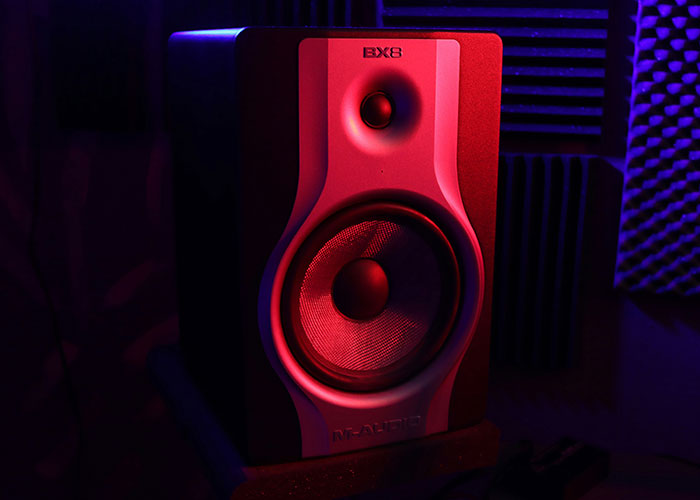 Studio monitor speaker illuminated with red and purple lighting, emphasizing sound equipment in a dark room setting. Studio monitor speaker illuminated with red and purple lighting, emphasizing sound equipment in a dark room setting.