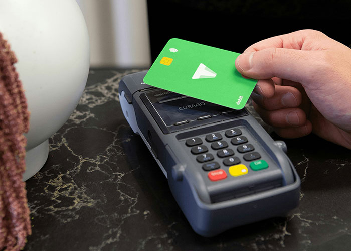 Hand holding green debit card tapping on payment terminal, illustrating things people can't believe they had to explain.