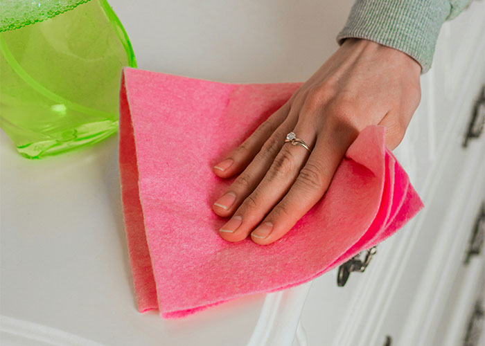 Hand wiping surface with pink cloth and green cleaning spray, illustrating things people can't believe they had to explain.