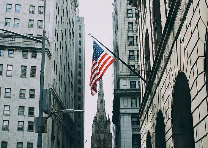Urban city street scene with an American flag between tall buildings, illustrating things people can't believe they had to explain.