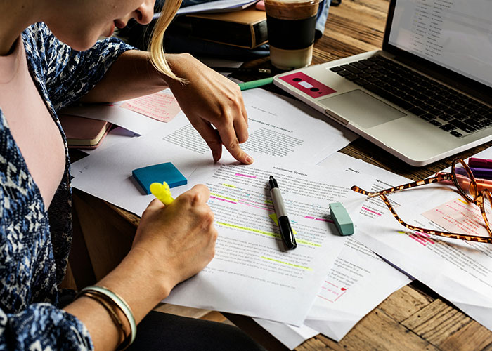 Person highlighting and explaining text on printed sheets with laptop and stationery, illustrating things people can't believe.