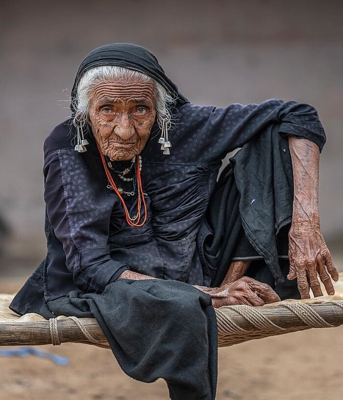 Elderly person with detailed wrinkles wearing traditional black clothing, captured in a striking portrait by Massimo Bietti.